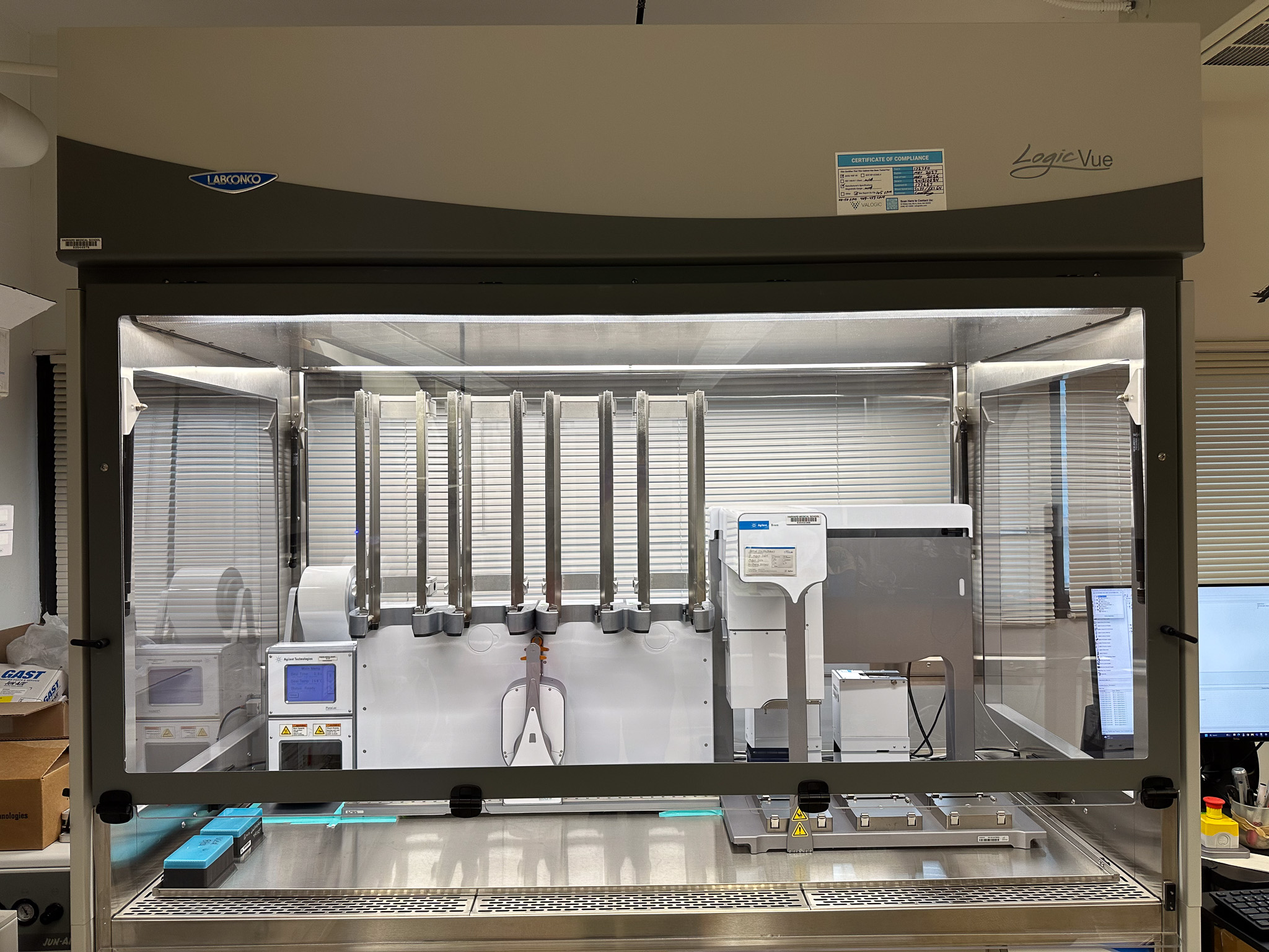 A large biosafety cabinet that has the automation platform of Agilent PlateLoc, BenchCel, and Bravo (left to right) inside